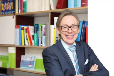 Ein lächelnder Mann in Anzug und Brille steht mit verschränkten Armen vor einem bunten Bücherregal und ist bereit, seine SEO-Fallstudie vorzustellen.