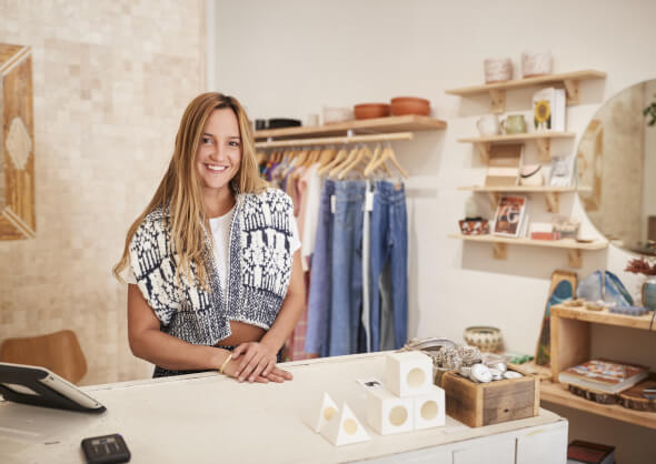 Lächelnde Frau hinter der Theke einer Boutique, die den Charme eines kleinen Unternehmens zur Schau stellt – ideale Inspiration für lokales SEO und Shop-Optimierung.