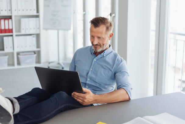 Man mit Bart und kurzen Haaren arbeitete entspannt am Laptop an einer SEO-Analyse in modernem, hellem Büro.