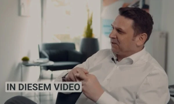 Mann im weißen Hemd gestikuliert im modernen Büro, spricht SEO Agentur Köln; Text „IN DIESEM VIDEO“ unten links.