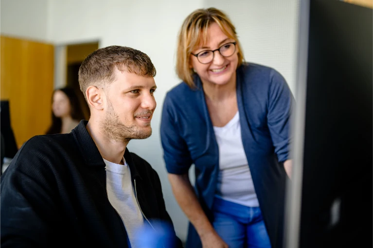 Ein lächelnder Mann und eine lächelnde Frau schauen gemeinsam in einem Büro auf einen Computerbildschirm.