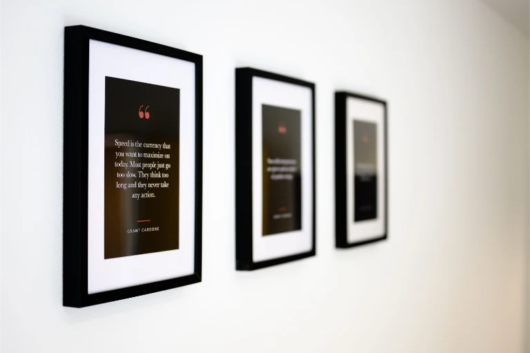 Drei gerahmte Motivationszitate hängen in einer Reihe an einer weißen Wand, wobei nur der nächstgelegene Rahmen scharf zu sehen ist.