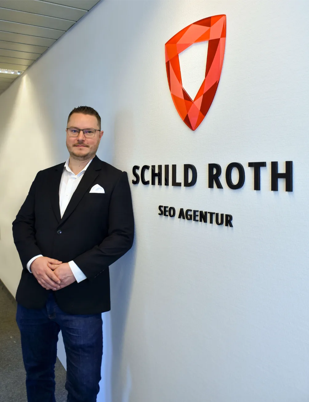 Ein Mann im Anzug steht an einer Wand mit dem Logo „SCHILD ROTH SEO AGENTUR“ und betont die SEO-Kompetenz für Anwälte.