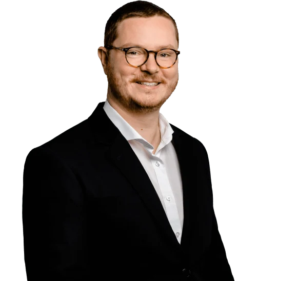 Mann mit braunen Haaren und Brille lächelt im Anzug vor neutralem Hintergrund – ideal für SEO-Team-Präsentationen.